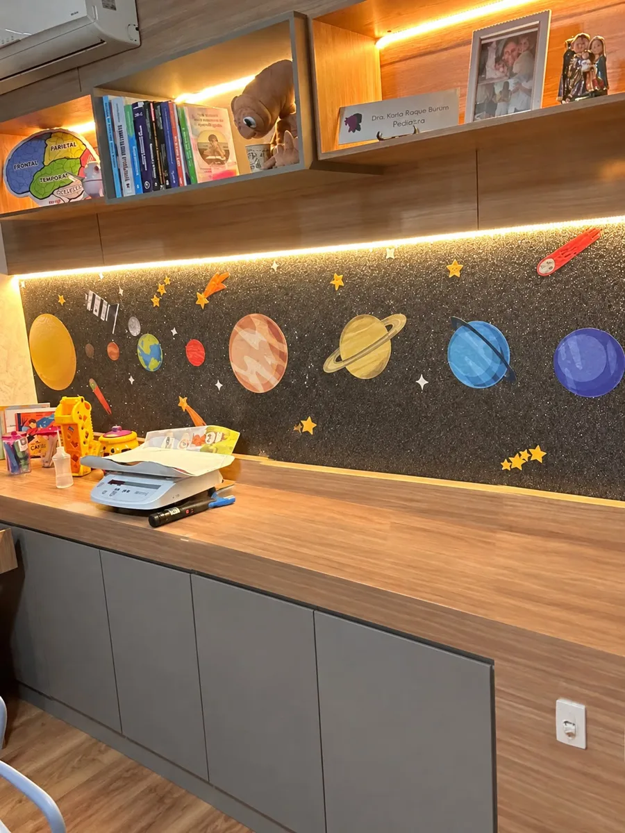Consultório pediátrico da Diverte e Desenvolve com bancada de madeira, balança infantil e parede decorada com os planetas do sistema solar